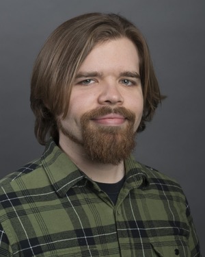 professor in a blue and green plaid button up shirt in front of a grey backdrop